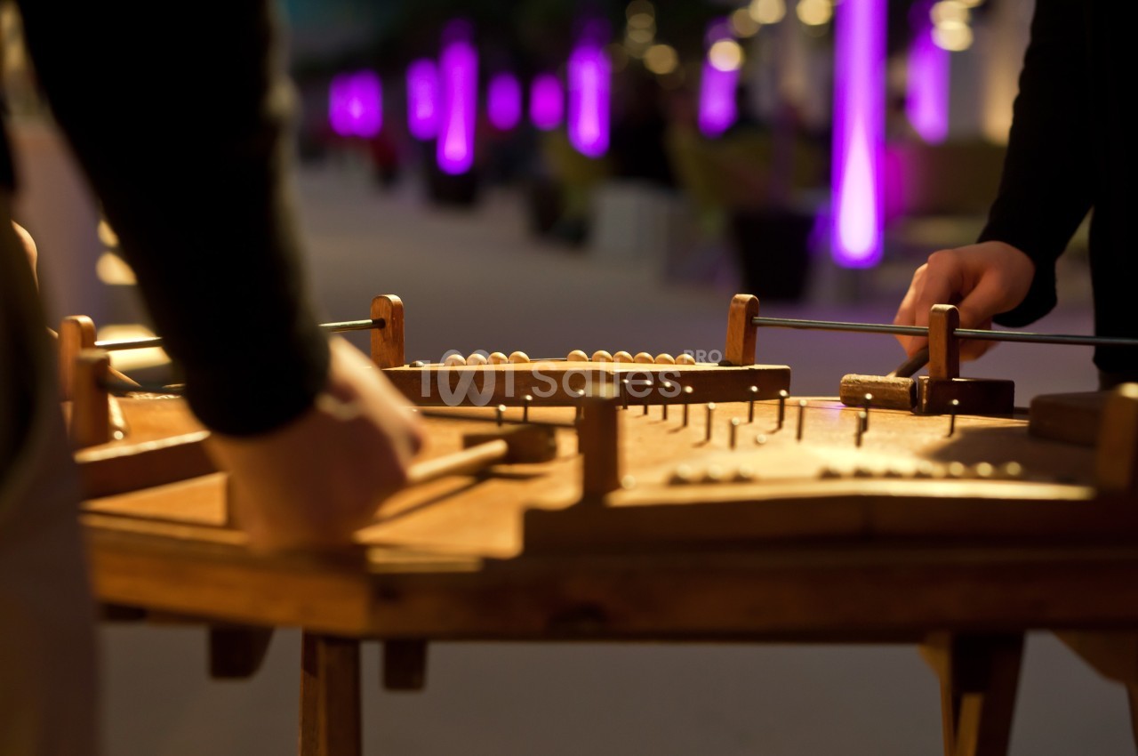 Personnes jouant d'un instrument de musique à cordes sur une table en bois, éclairées par des lumières violettes en arrière…