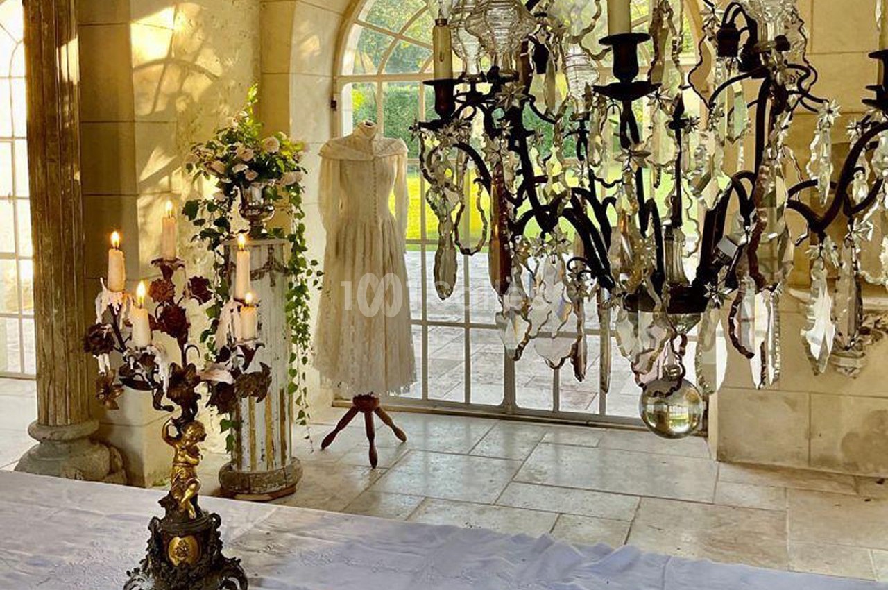 Robe blanche sur un mannequin près d'une fenêtre, entourée de chandeliers et de décorations florales dans une salle…