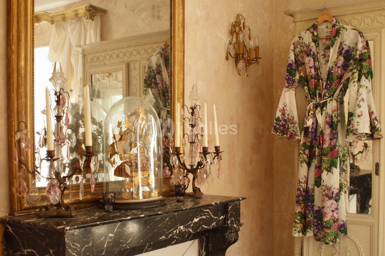Manteau à motifs floraux suspendu près d'une armoire, avec un miroir doré et des chandeliers sur une cheminée en marbre.