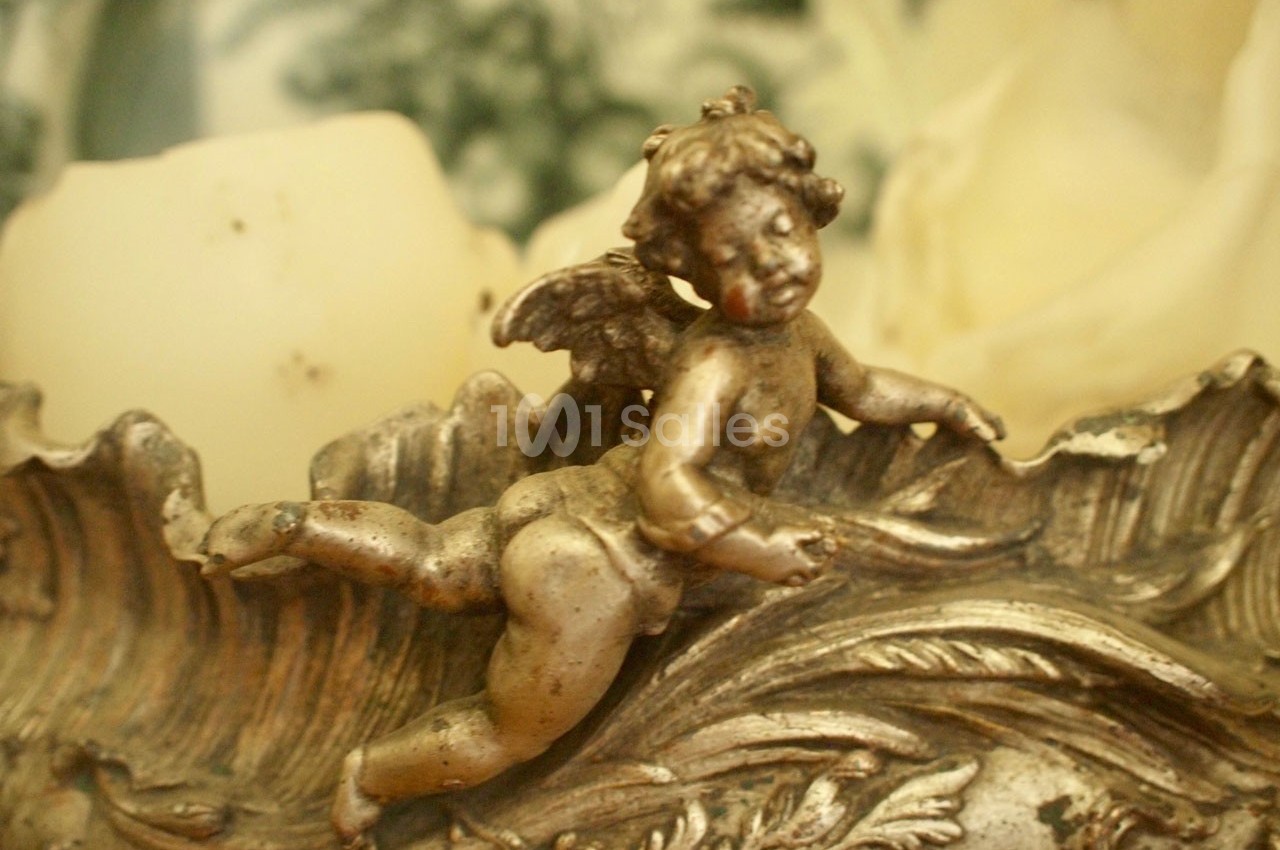 Statue en métal représentant un ange ailé allongé sur un décor ornemental aux détails sculptés.