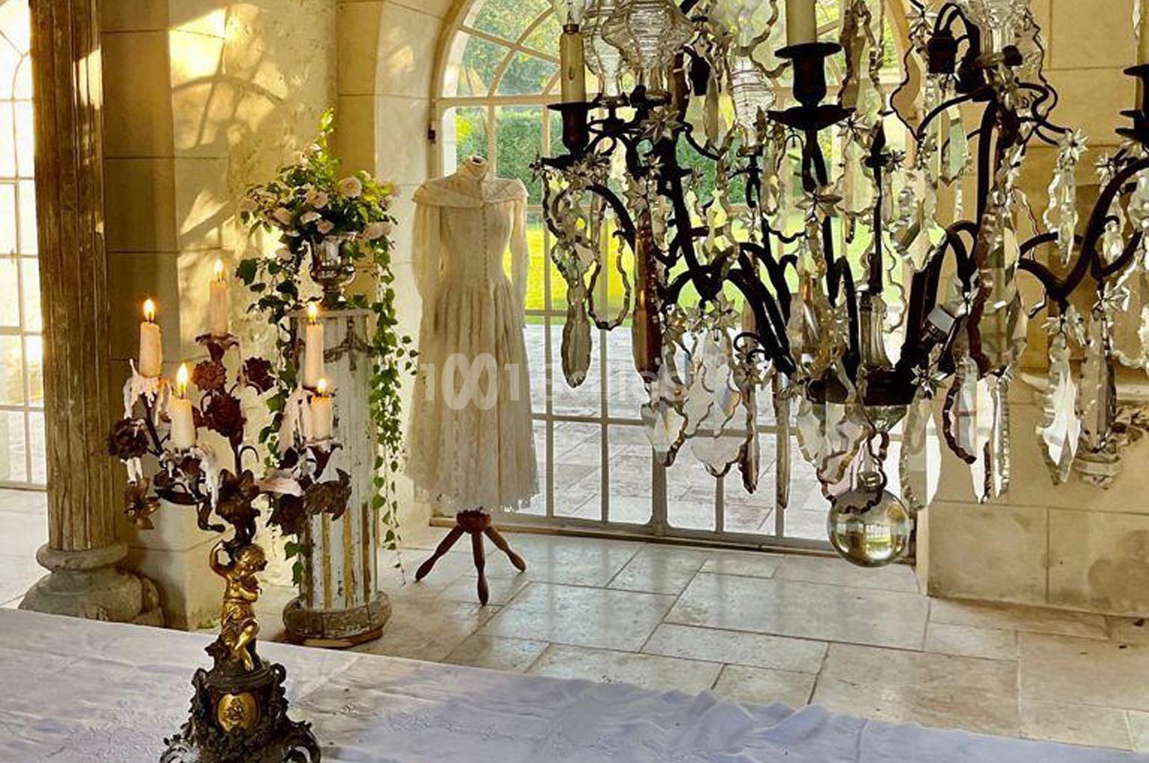 Robe blanche sur un mannequin près d'une fenêtre, entourée de chandeliers et de décorations florales dans une pièce…