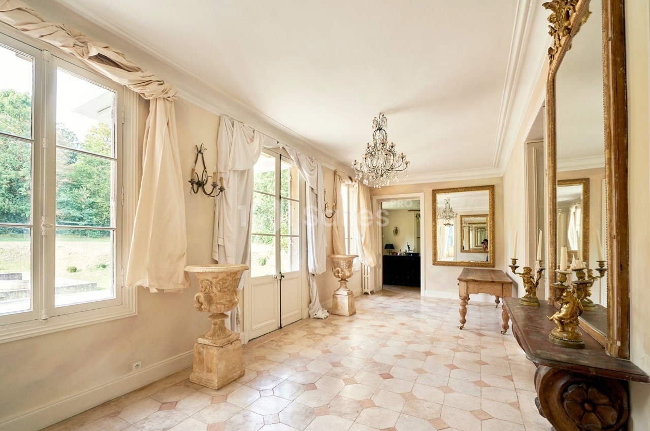Salle lumineuse avec sol en carreaux clairs, grandes fenêtres, miroirs dorés, chandeliers et décorations classiques.