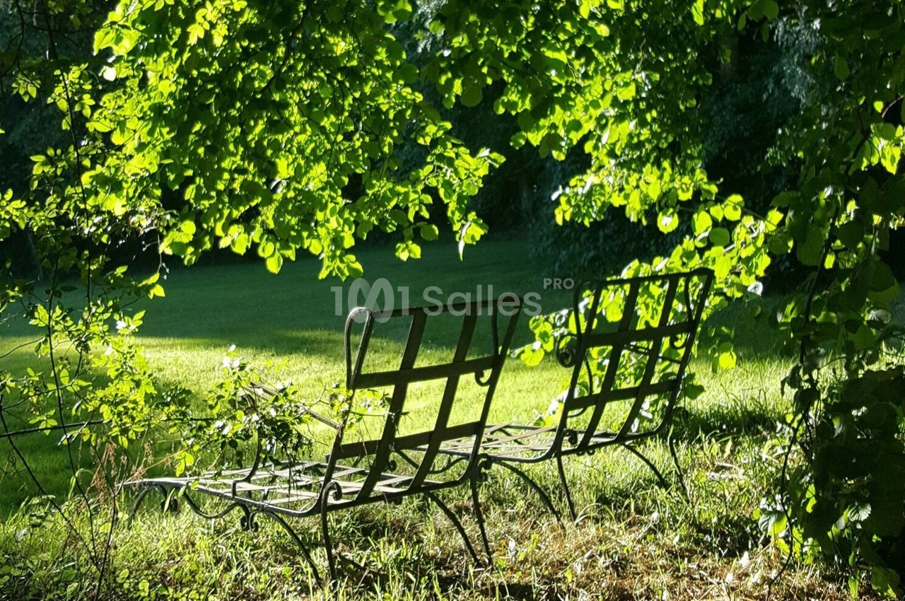 Deux chaises en métal sont placées sur une pelouse ensoleillée, entourées de verdure et d'ombres d'arbres.