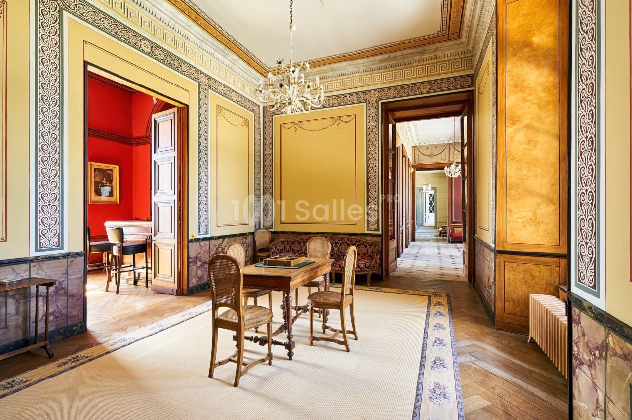 Salle élégante avec parquet en bois, murs ornés de moulures, lustres et mobilier classique.