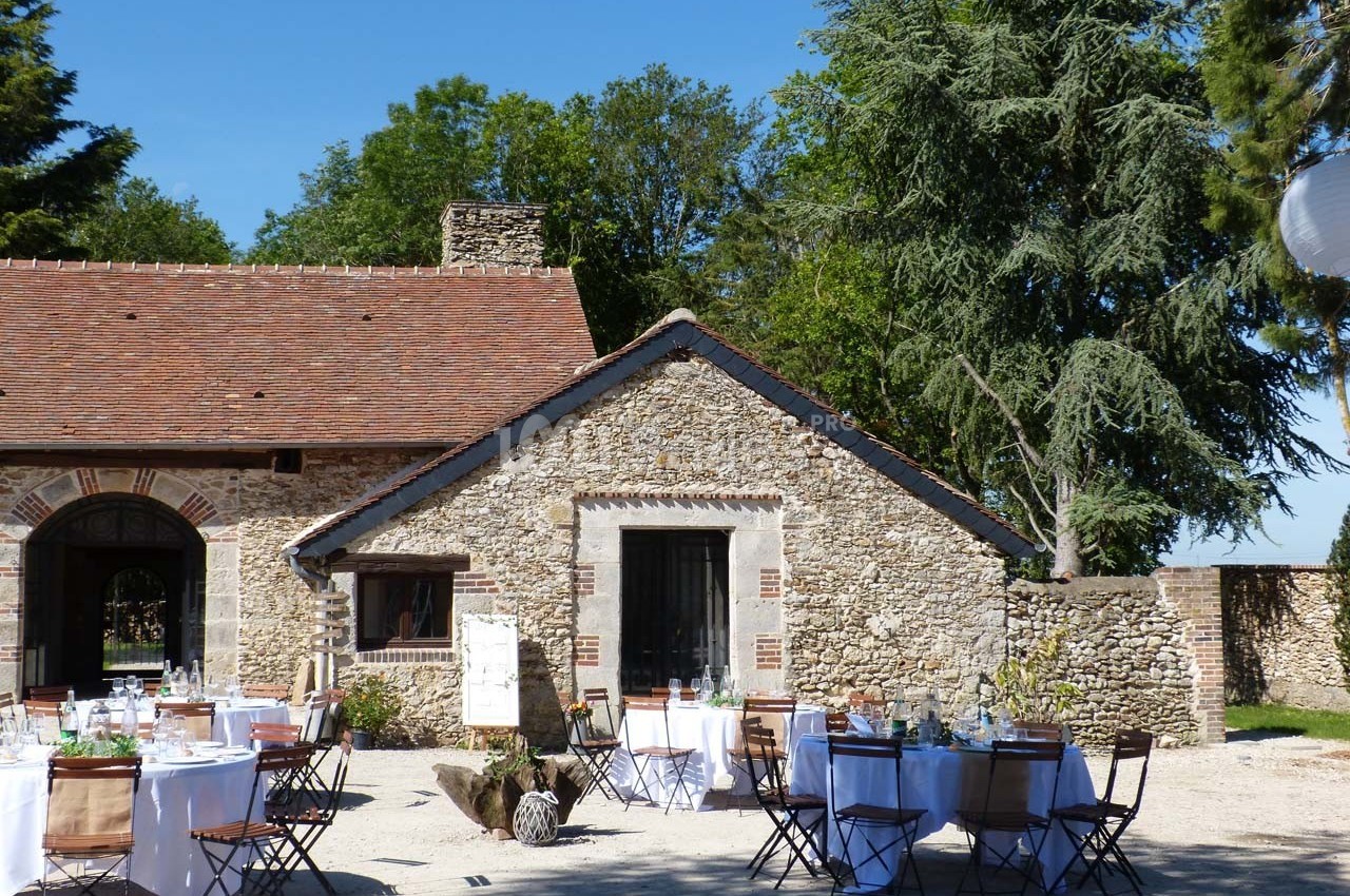 Cour extérieure avec tables dressées pour un événement devant un bâtiment en pierre sous un ciel dégagé.
