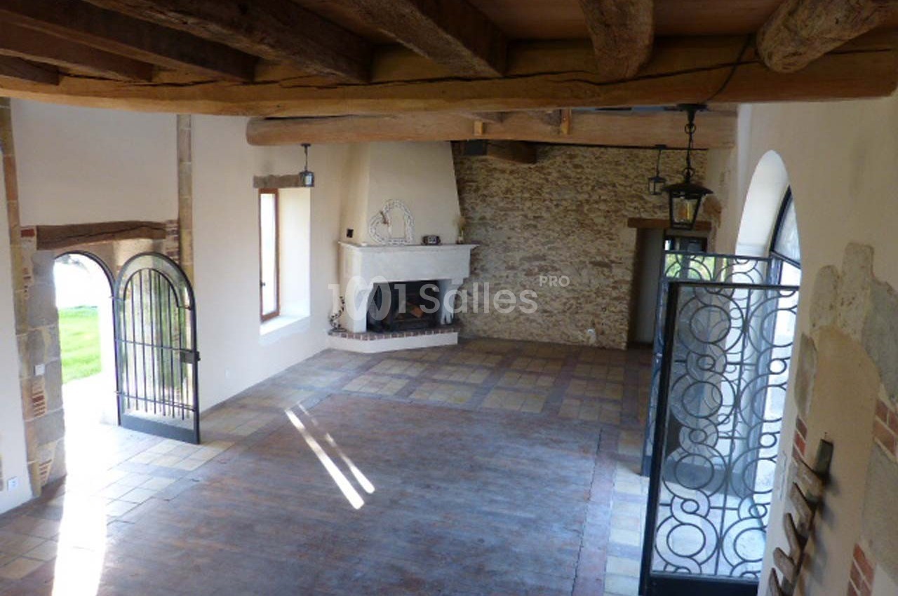 Salle lumineuse avec poutres apparentes, cheminée en pierre, sol en carrelage et parquet, et portes en fer forgé.