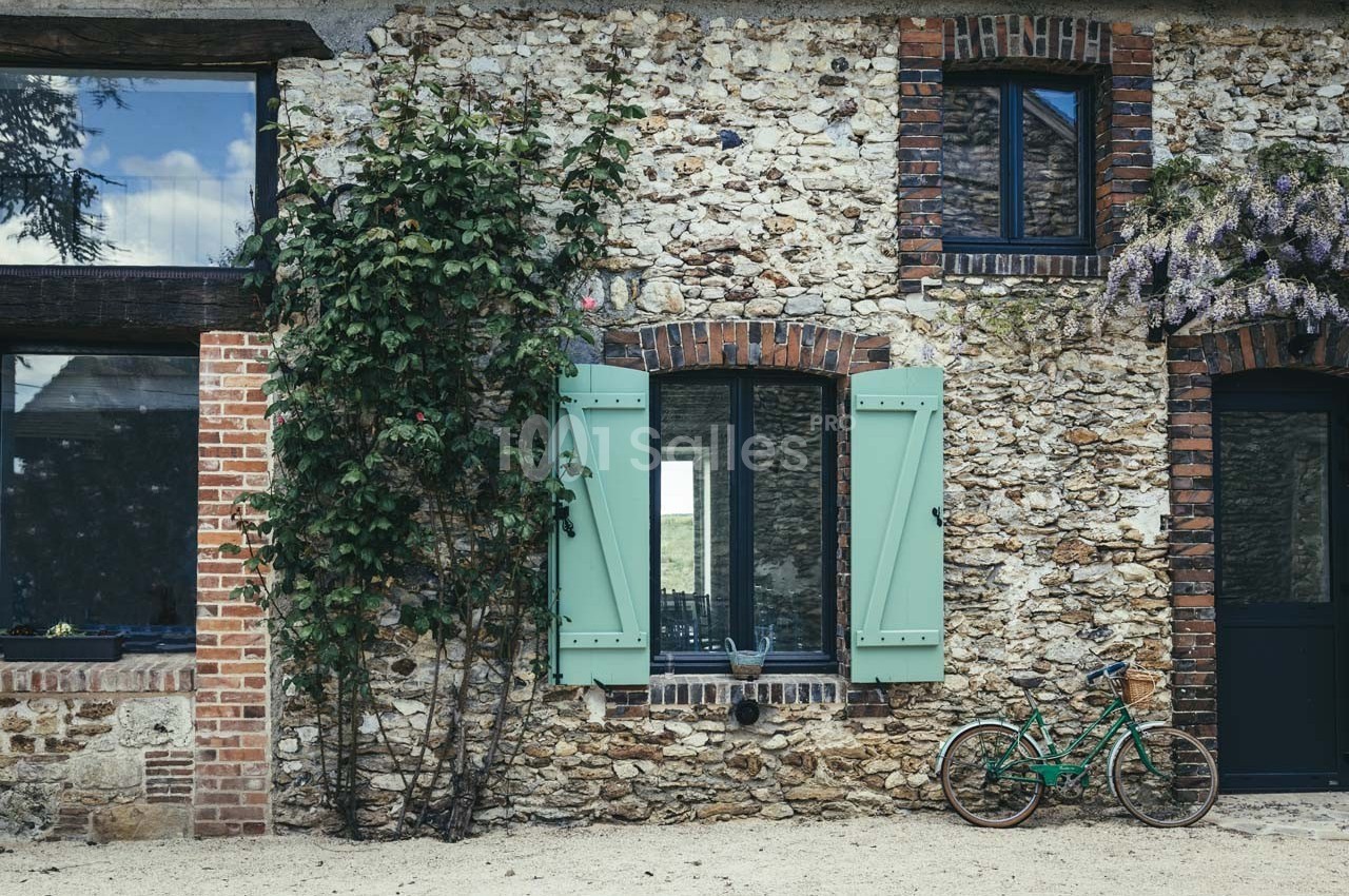 Façade en pierre avec volets verts, une vigne grimpante et un vélo vert posé près de la porte.