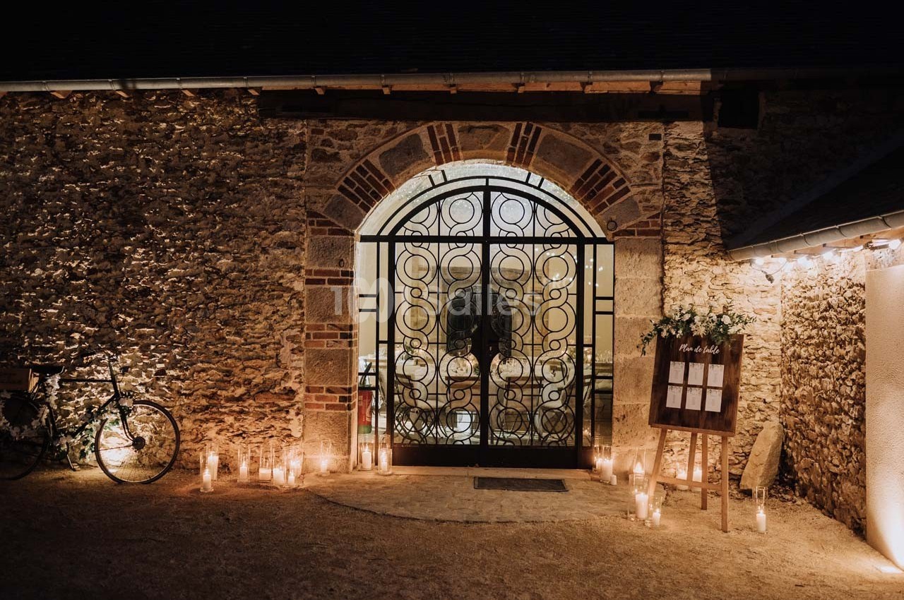 Entrée d'un bâtiment en pierre avec une porte en fer forgé, entourée de bougies et d'une décoration lumineuse.