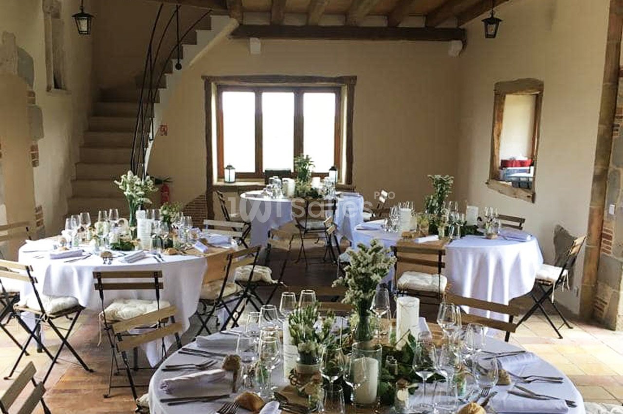 Salle décorée pour un événement avec tables rondes dressées, nappes blanches et arrangements floraux.