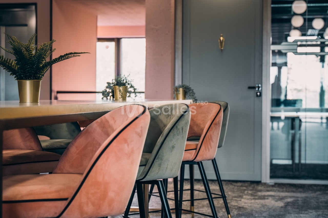 Chaises rembourrées roses et vertes autour d'une table en bois dans un espace intérieur lumineux et moderne.