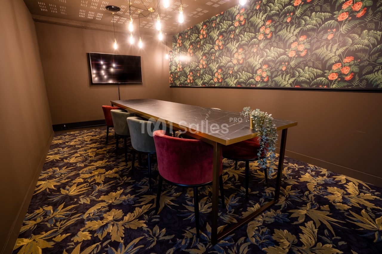 Salle de réunion avec table en marbre, chaises colorées, mur décoré de motifs floraux et éclairage suspendu.