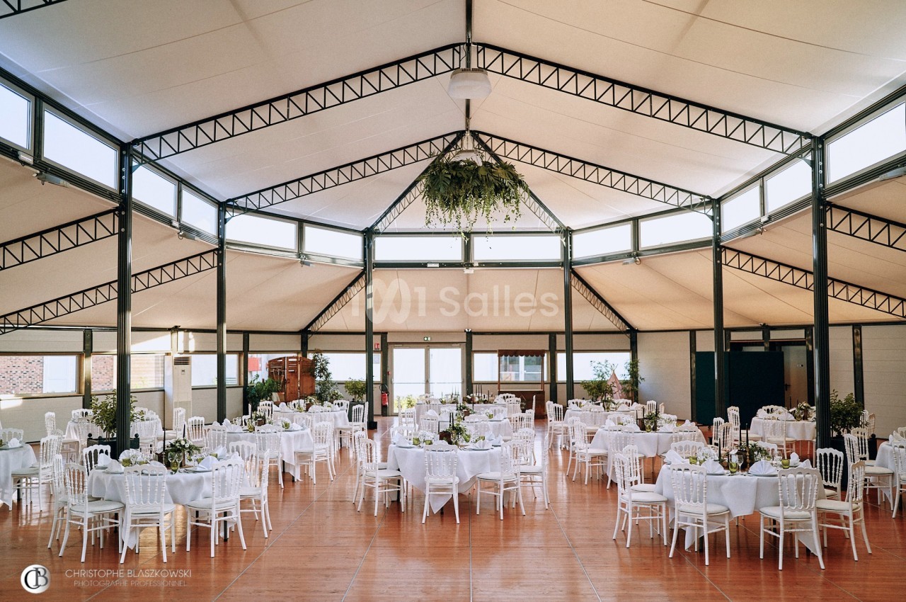Salle de réception lumineuse avec des tables rondes décorées de nappes blanches et des chaises assorties.