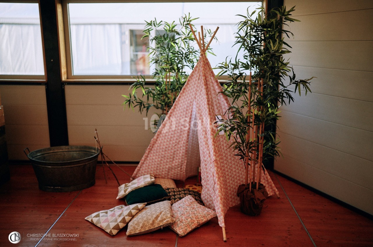 Tente décorative en tissu géométrique entourée de plantes en pot, avec des coussins colorés posés au sol.