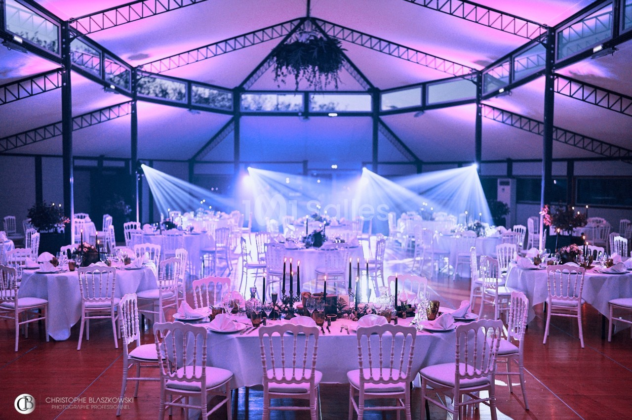 Salle de réception décorée avec des tables dressées, éclairage tamisé et projecteurs lumineux.