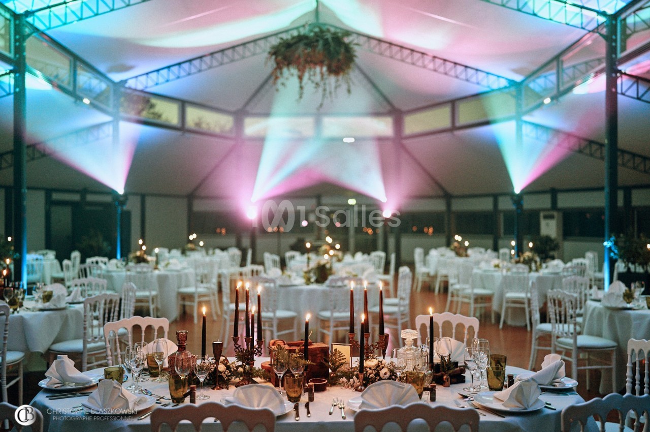 Salle de réception décorée avec des tables dressées, éclairage coloré et centre de table floral.