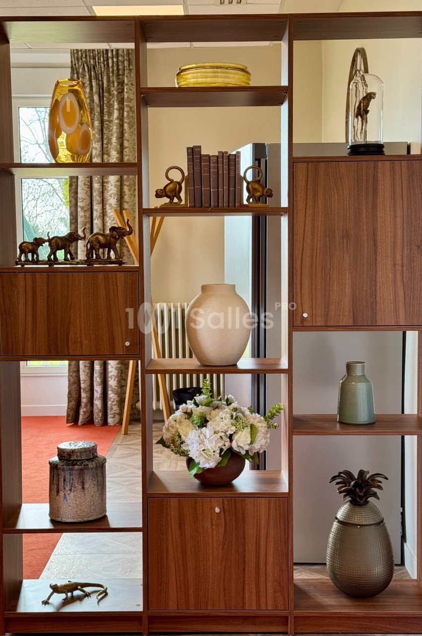 Étagère en bois avec objets décoratifs variés, dont vases, livres, figurines et plantes, dans une pièce lumineuse.