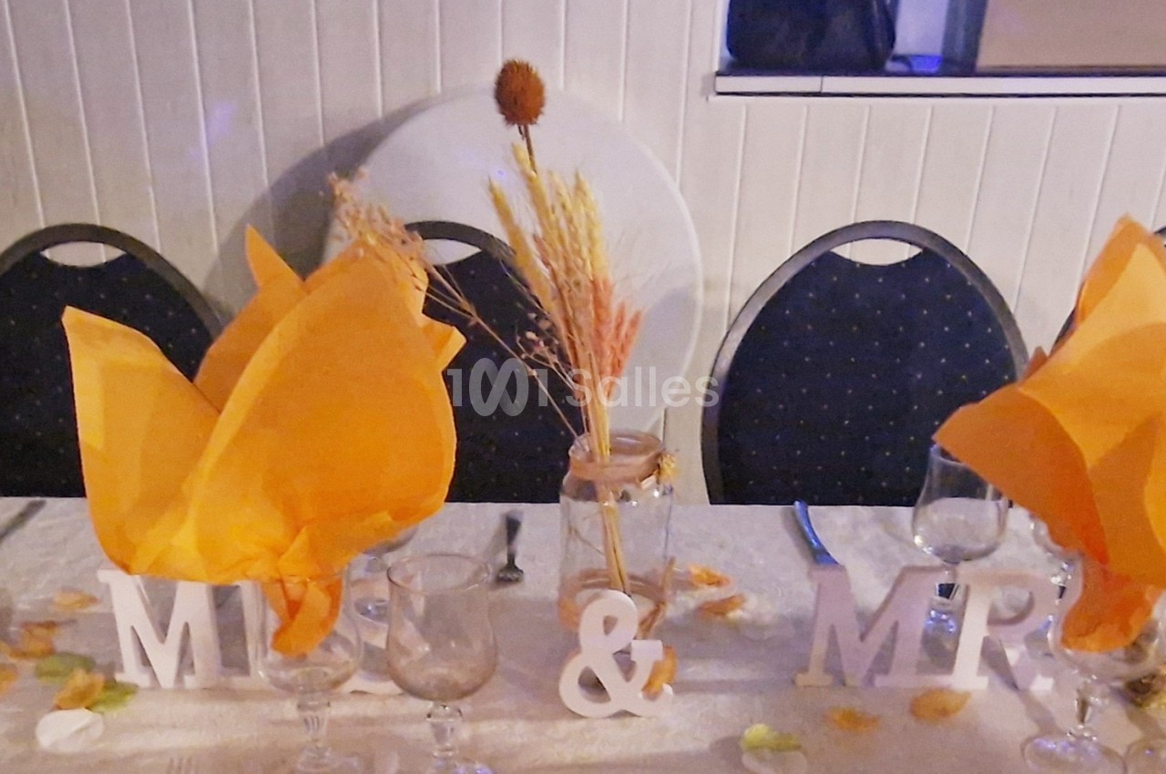 Table décorée pour un mariage avec serviettes orange pliées, vase de fleurs séchées et lettres ’Mr & Mrs’.