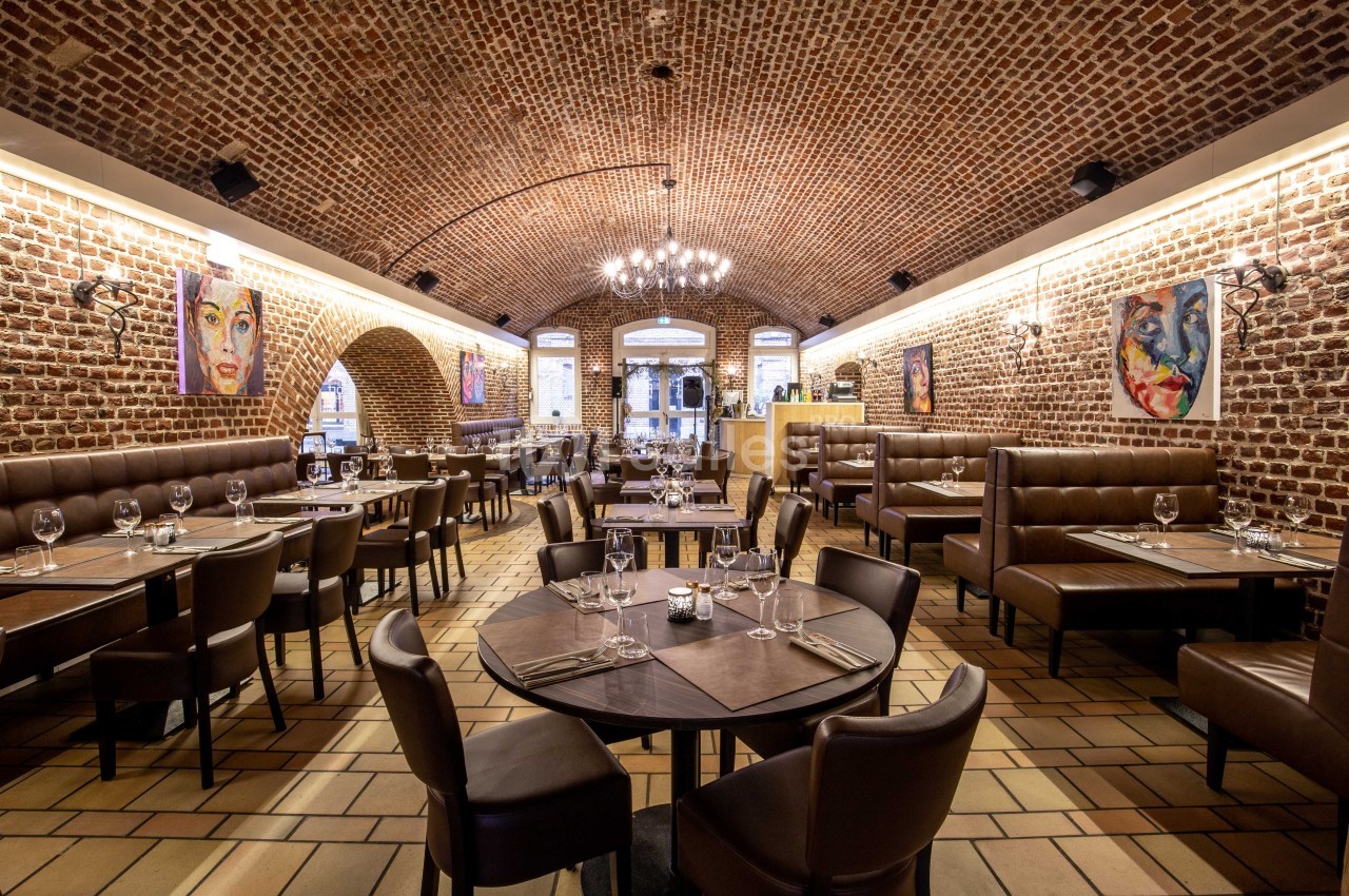 Salle de restaurant avec voûtes en briques, tables dressées et peintures colorées accrochées aux murs.