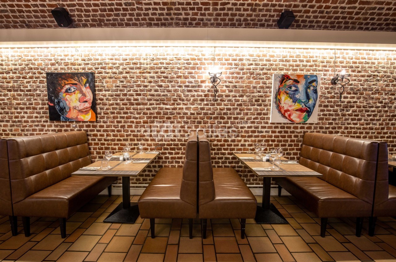 Banquettes en cuir marron dans un restaurant avec murs en briques, tableaux colorés et tables dressées.