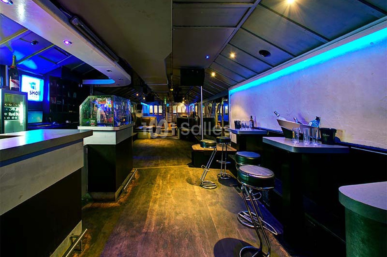 Intérieur d'un bar avec comptoir, tabourets hauts, éclairage tamisé et néons bleus sur les murs.