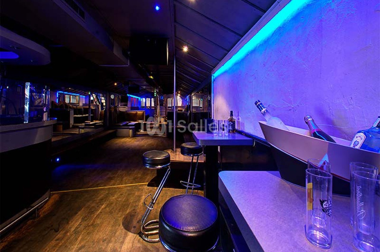 Intérieur d'un bar ou club avec comptoir, tabourets, bouteilles et éclairage bleu tamisé.