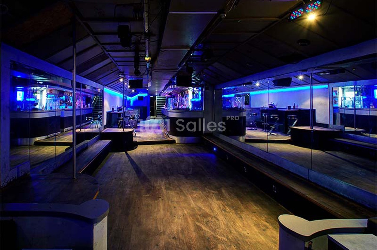 Salle de club vide avec éclairage bleu, miroirs sur les murs et bar en arrière-plan.