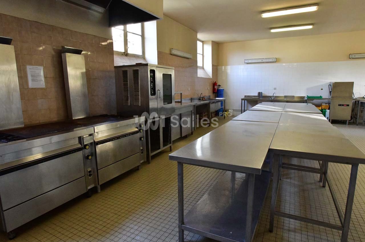 Cuisine professionnelle avec plans de travail en inox, équipements de cuisson et carrelage au sol beige.