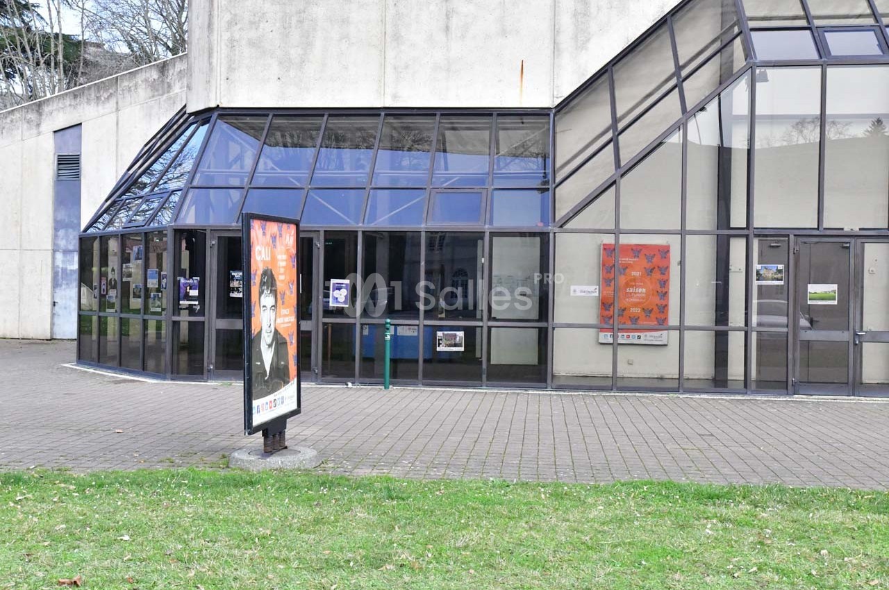 Façade vitrée d'un bâtiment public avec affiches promotionnelles visibles sur les murs et un panneau publicitaire extérieur.