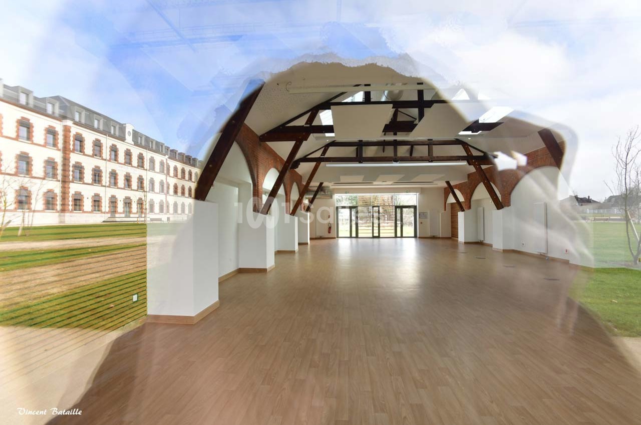 Salle lumineuse avec parquet, poutres apparentes et grandes baies vitrées donnant sur un espace extérieur verdoyant.