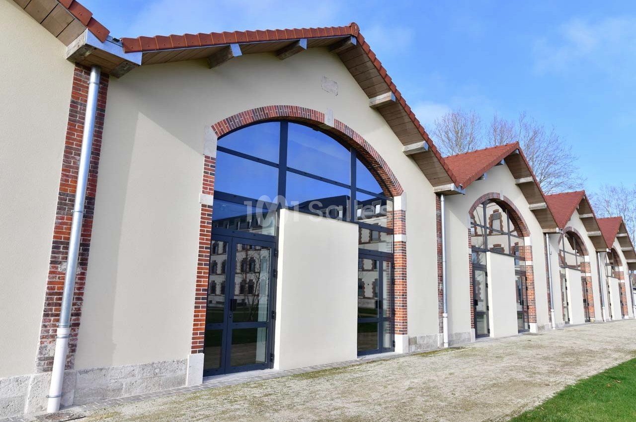 Façade d’un bâtiment rénové avec des arcs en briques, grandes baies vitrées et toits en tuiles rouges.