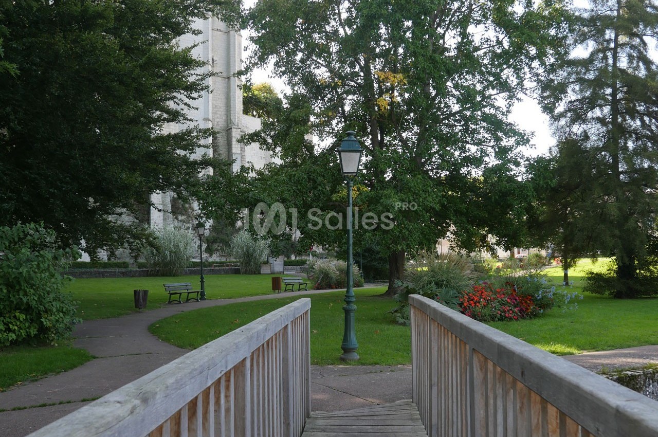 Passerelle en bois menant à un parc verdoyant avec lampadaire, bancs et arbres en arrière-plan.