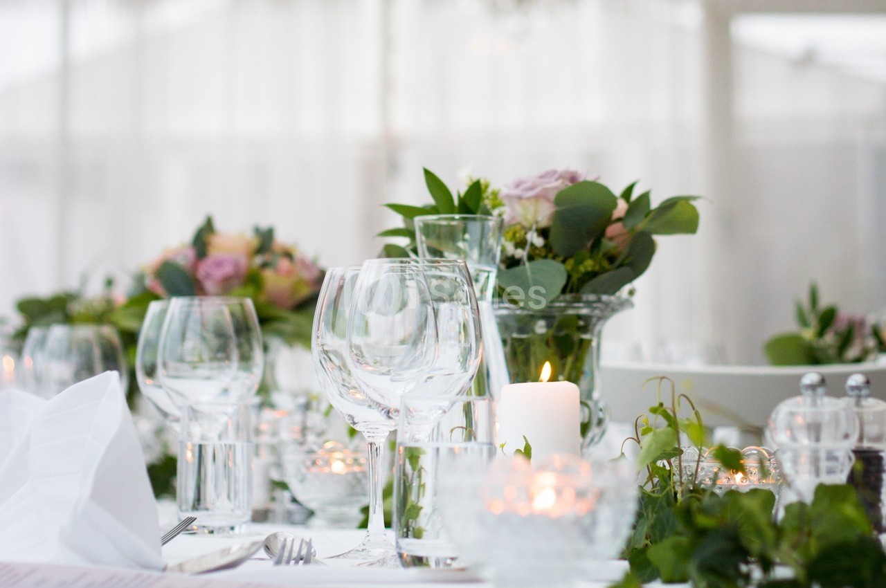 Table élégamment dressée avec verres, bougies allumées et compositions florales dans un cadre lumineux.
