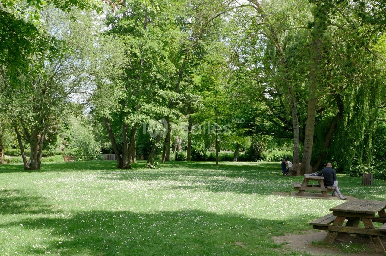Espace vert avec pelouse, arbres et tables de pique-nique, quelques personnes assises dans un cadre paisible.