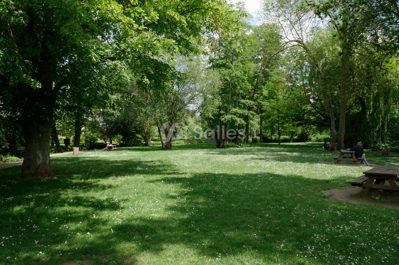 Pelouse verdoyante entourée d'arbres avec des bancs de pique-nique et des personnes profitant du parc.