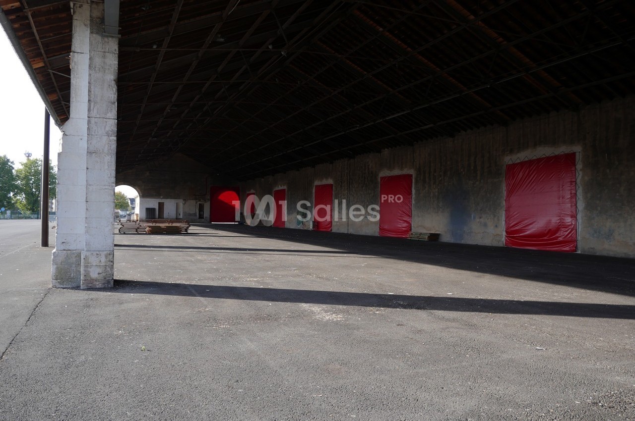 Hangar ouvert avec plusieurs portes rouges fermées, sol asphalté et structure en bois sous un toit incliné.