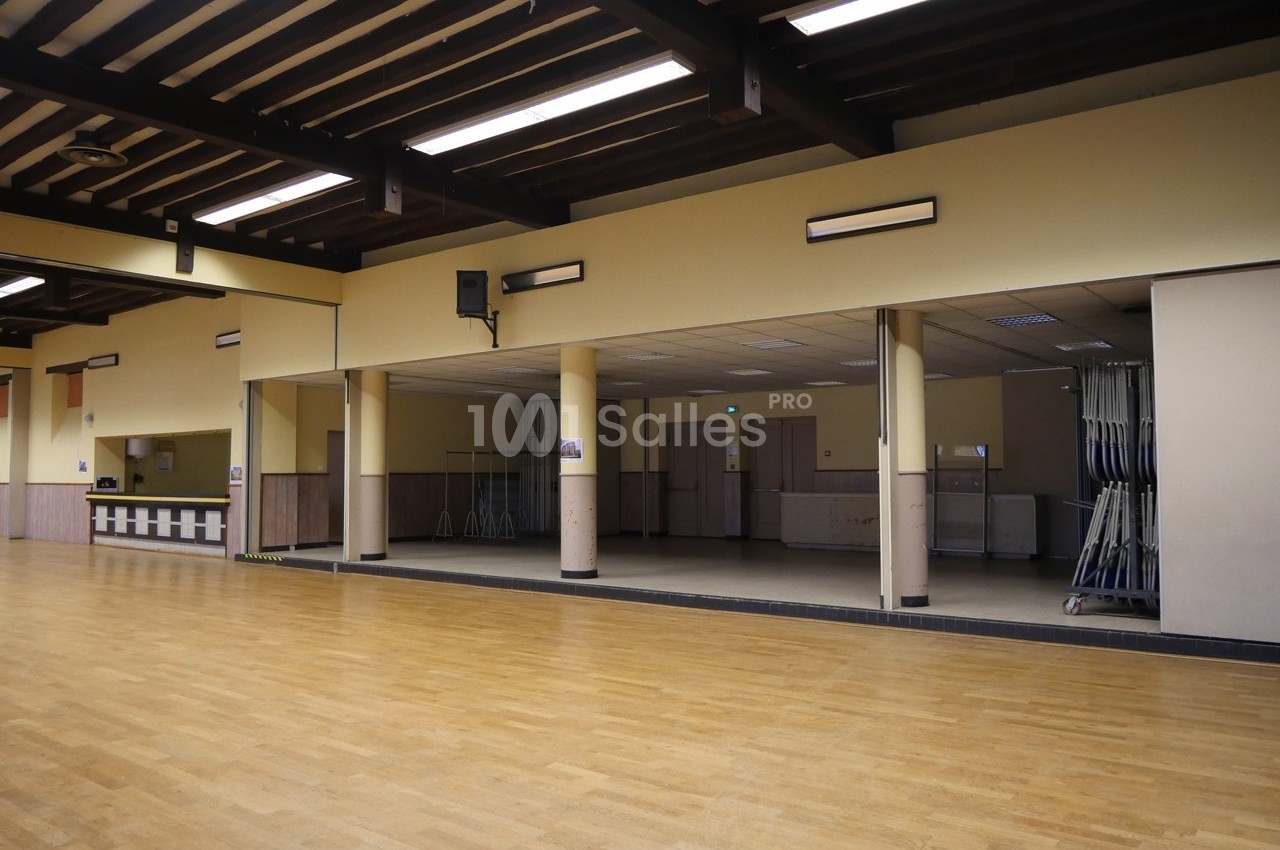 Salle spacieuse avec parquet en bois clair, murs beiges, miroirs et plafond à poutres apparentes.