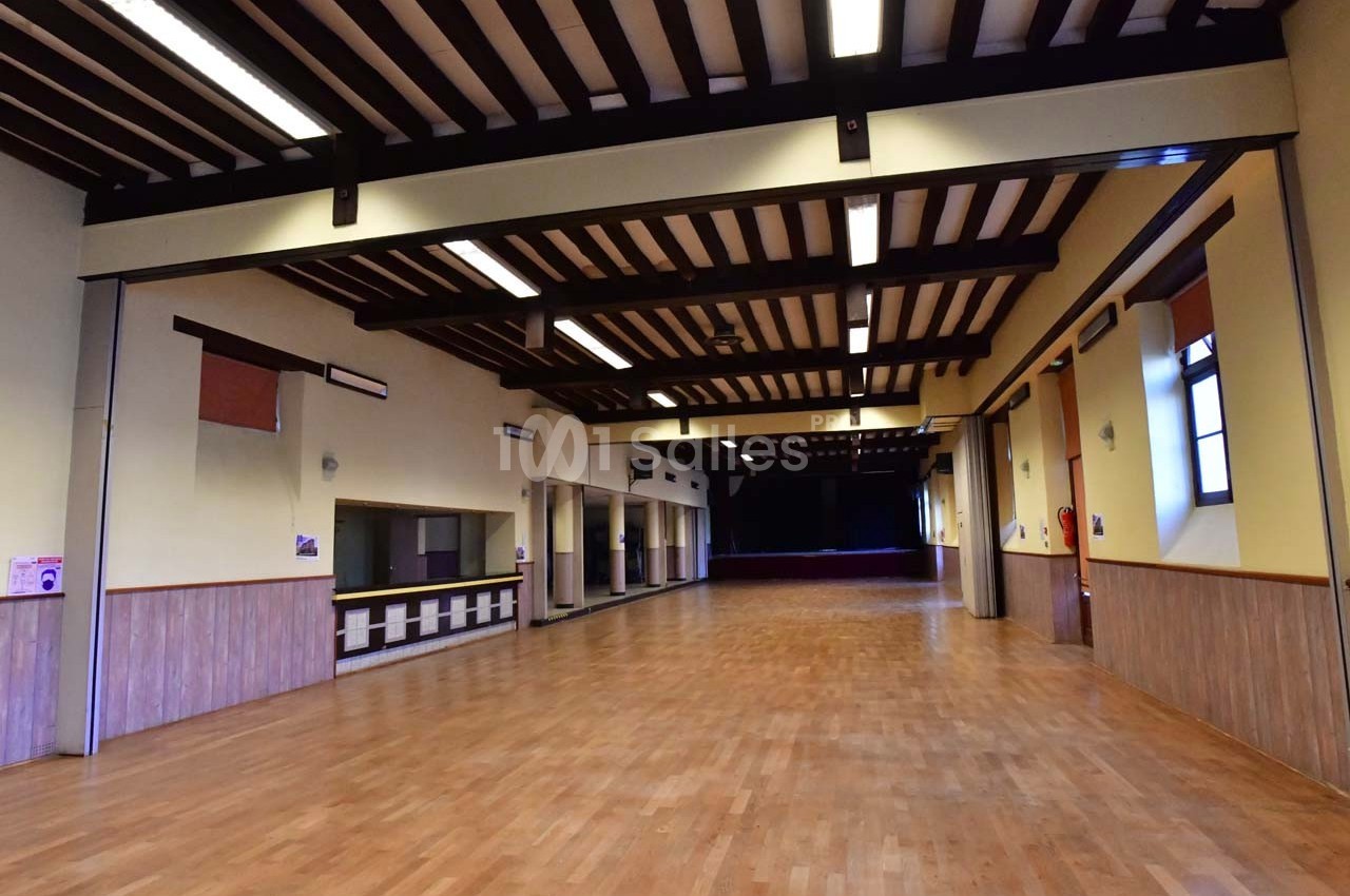 Salle spacieuse avec parquet en bois, murs jaunes, poutres apparentes et éclairage fluorescent.