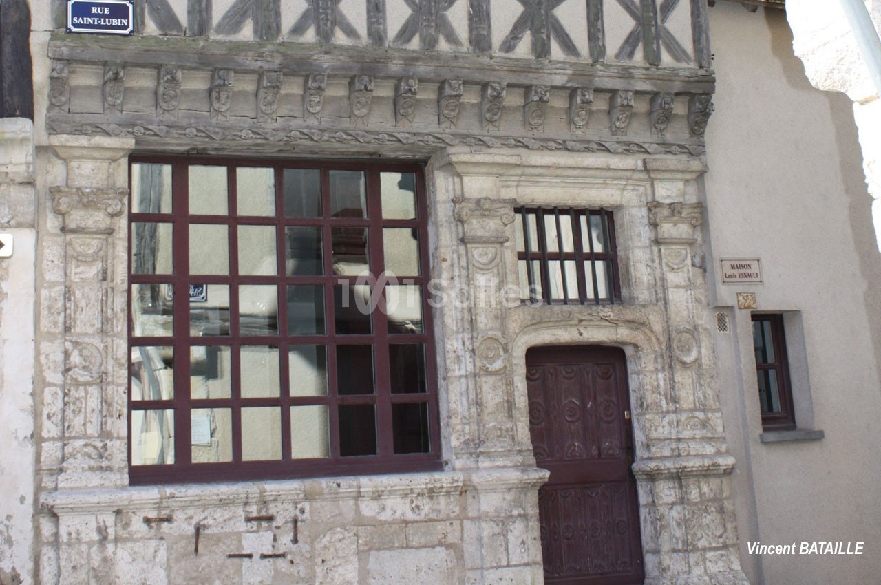 Façade en pierre d'une maison ancienne avec colombages, fenêtres à carreaux et porte sculptée.