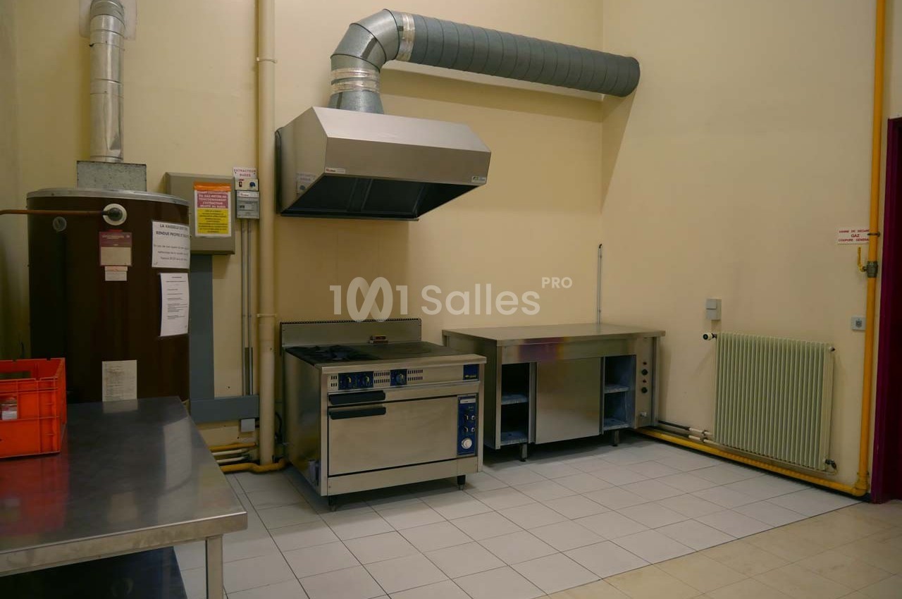 Cuisine professionnelle avec hotte, plaques de cuisson, plans de travail en inox et carrelage au sol.
