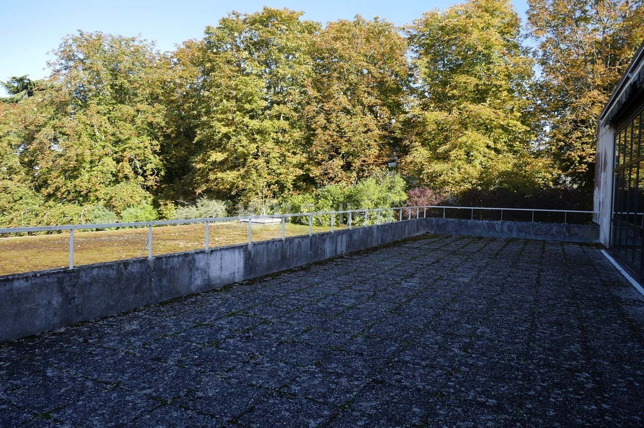 Terrasse en béton avec garde-corps métalliques, entourée d'arbres aux feuillages d'automne sous un ciel dégagé.