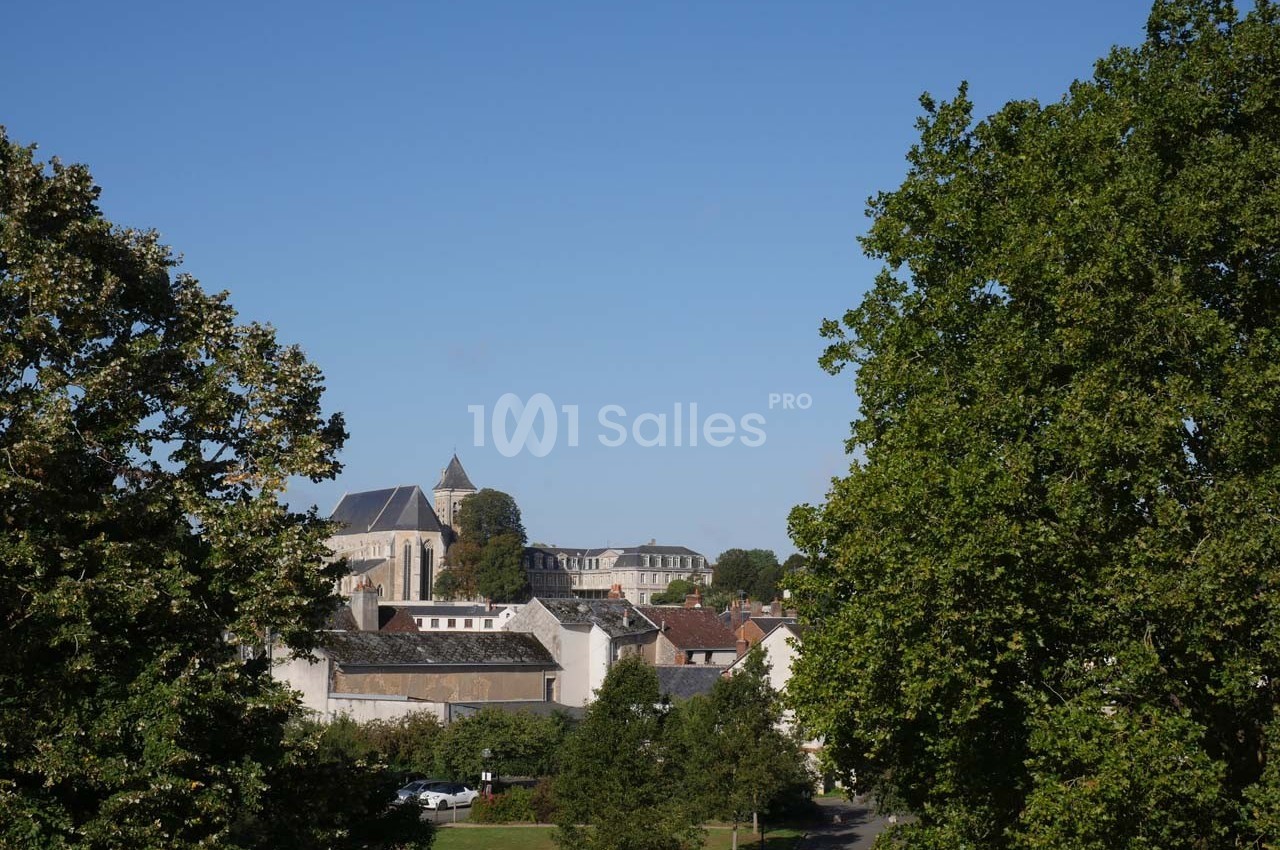 Vue d'un village avec une église au centre, entourée de bâtiments et d'arbres sous un ciel bleu clair.