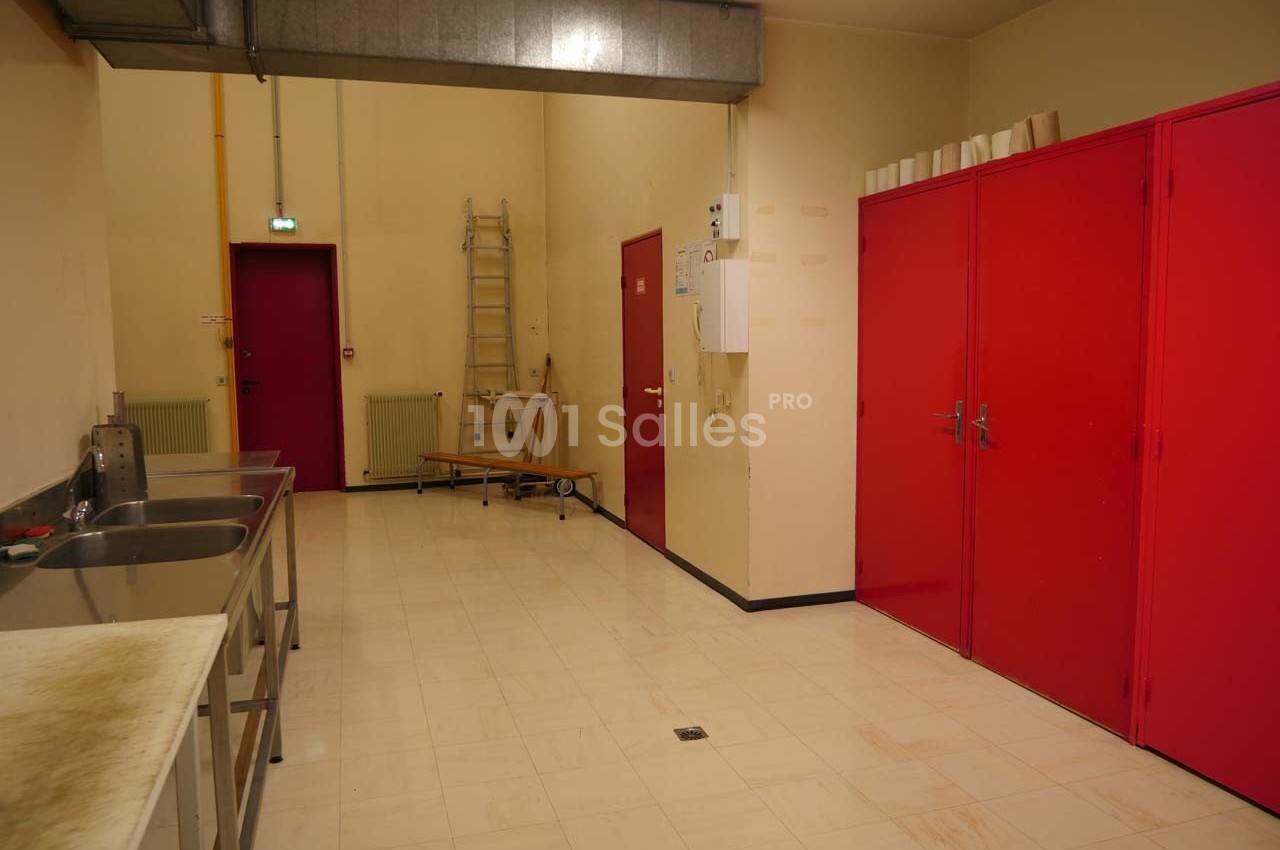 Salle de service avec éviers en inox, armoires rouges, échelle et murs beige clair.