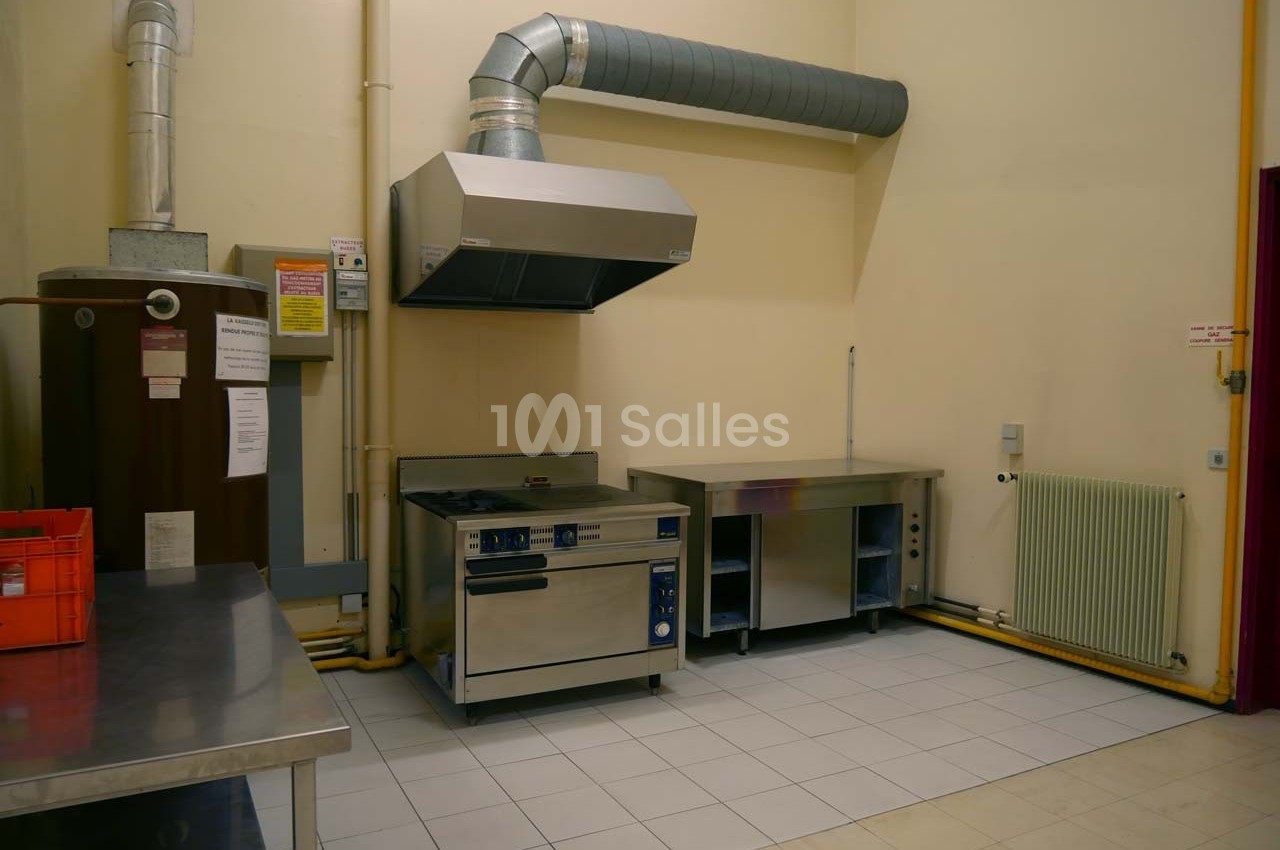 Cuisine professionnelle avec hotte, plaque de cuisson, plans de travail en inox et carrelage au sol.