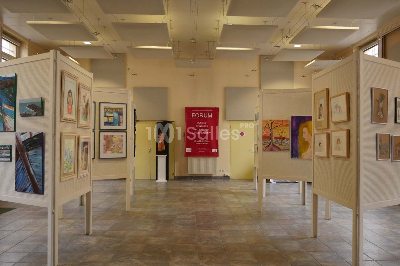 Salle d'exposition avec des panneaux affichant des peintures et dessins variés, éclairée par une lumière naturelle.