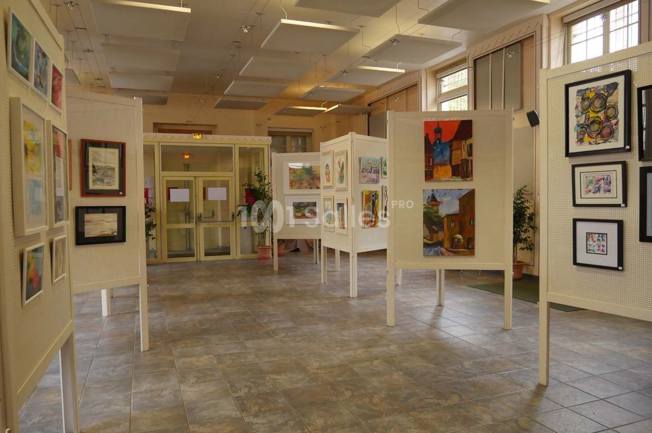 Salle d'exposition avec des peintures et dessins encadrés présentés sur des panneaux blancs.