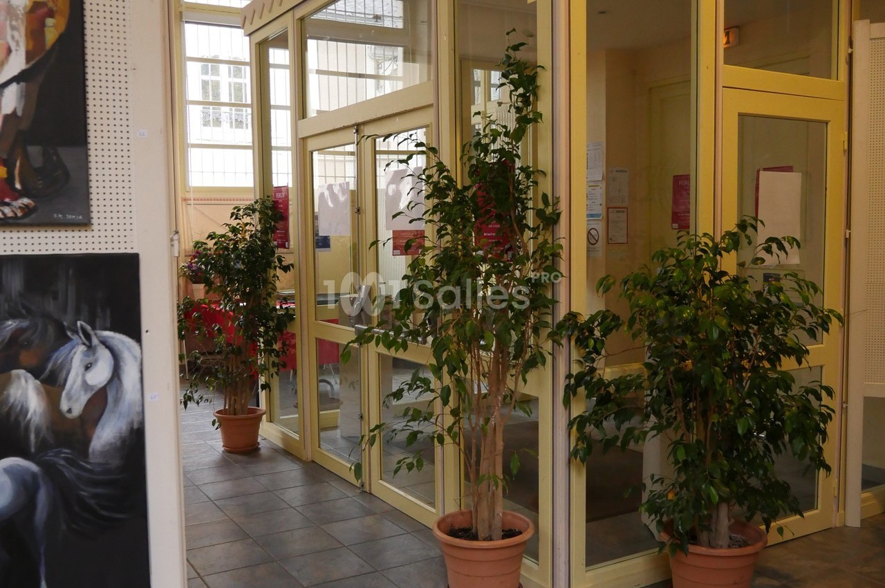 Entrée vitrée d'un bâtiment avec des plantes en pot et des peintures accrochées aux murs.