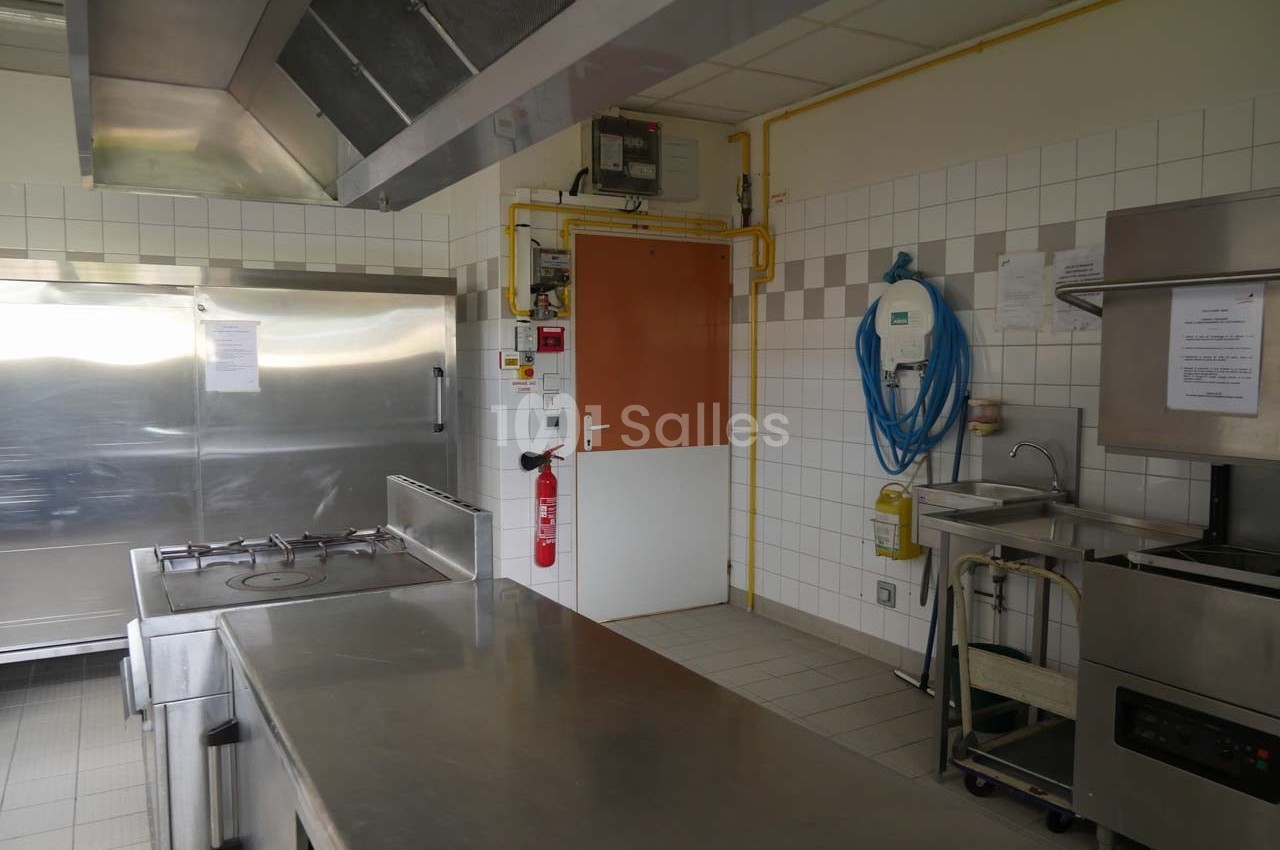 Cuisine professionnelle avec plans de travail en inox, équipements de cuisson, évier et murs carrelés blancs.