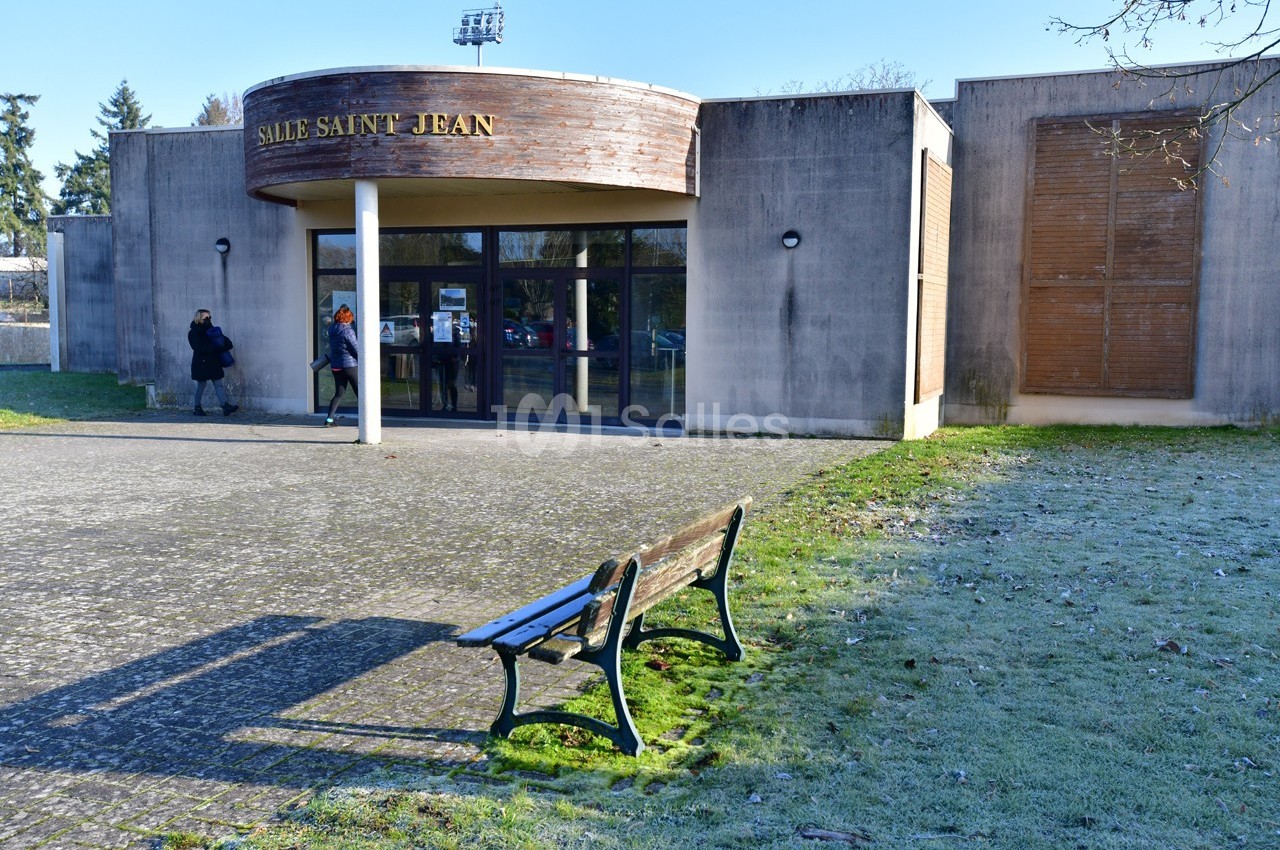 Banc en bois sur une place givrée devant un bâtiment nommé ’Salle Saint Jean’ avec des personnes entrant.