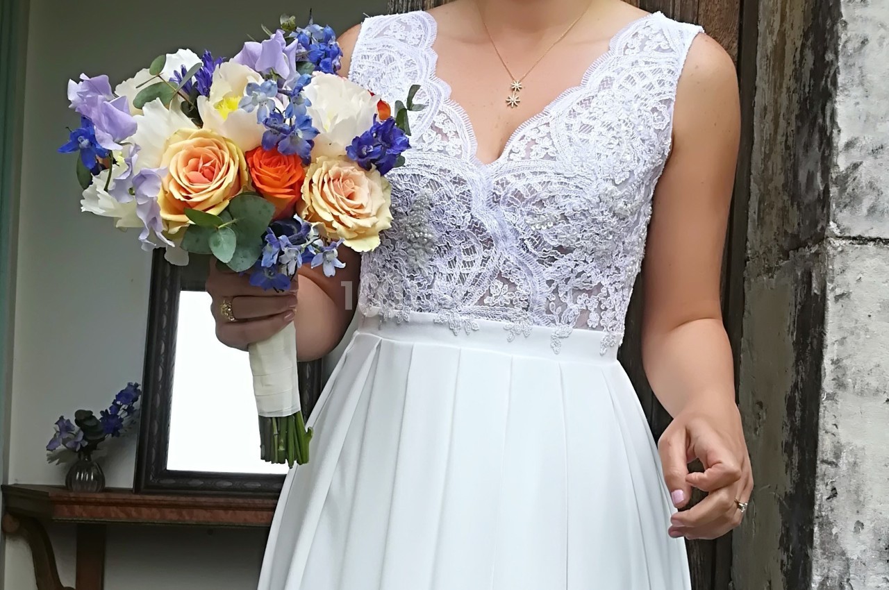 Femme en robe de mariée blanche tenant un bouquet coloré avec des roses, des fleurs violettes et bleues.