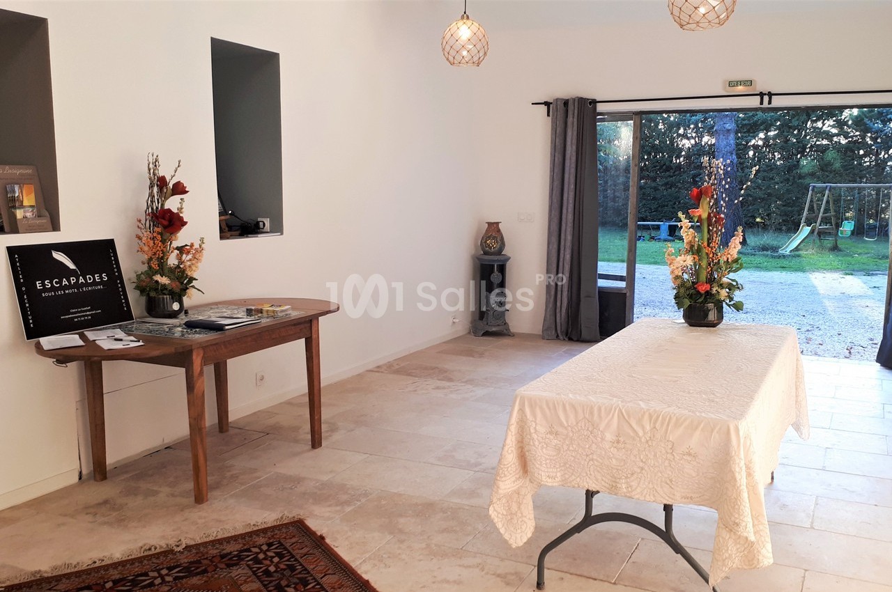 Salle lumineuse avec table décorée de fleurs, vue sur un jardin avec balançoire à travers une baie vitrée ouverte.